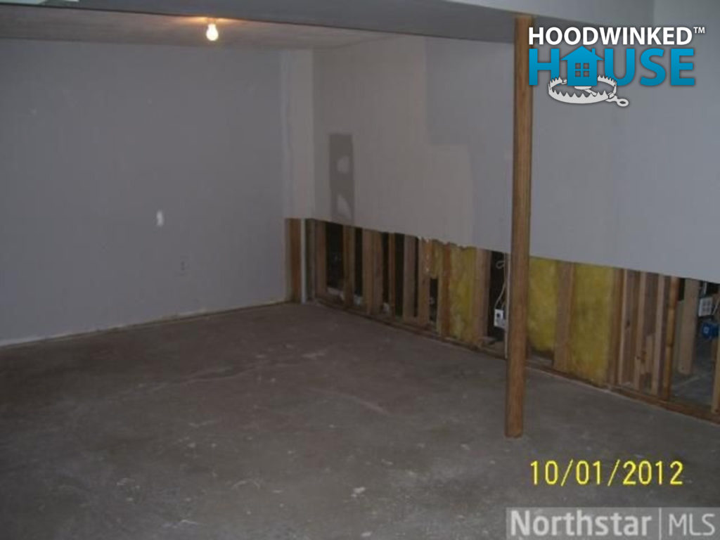 Basement with support column and partially demolished drywall from flood water damage.