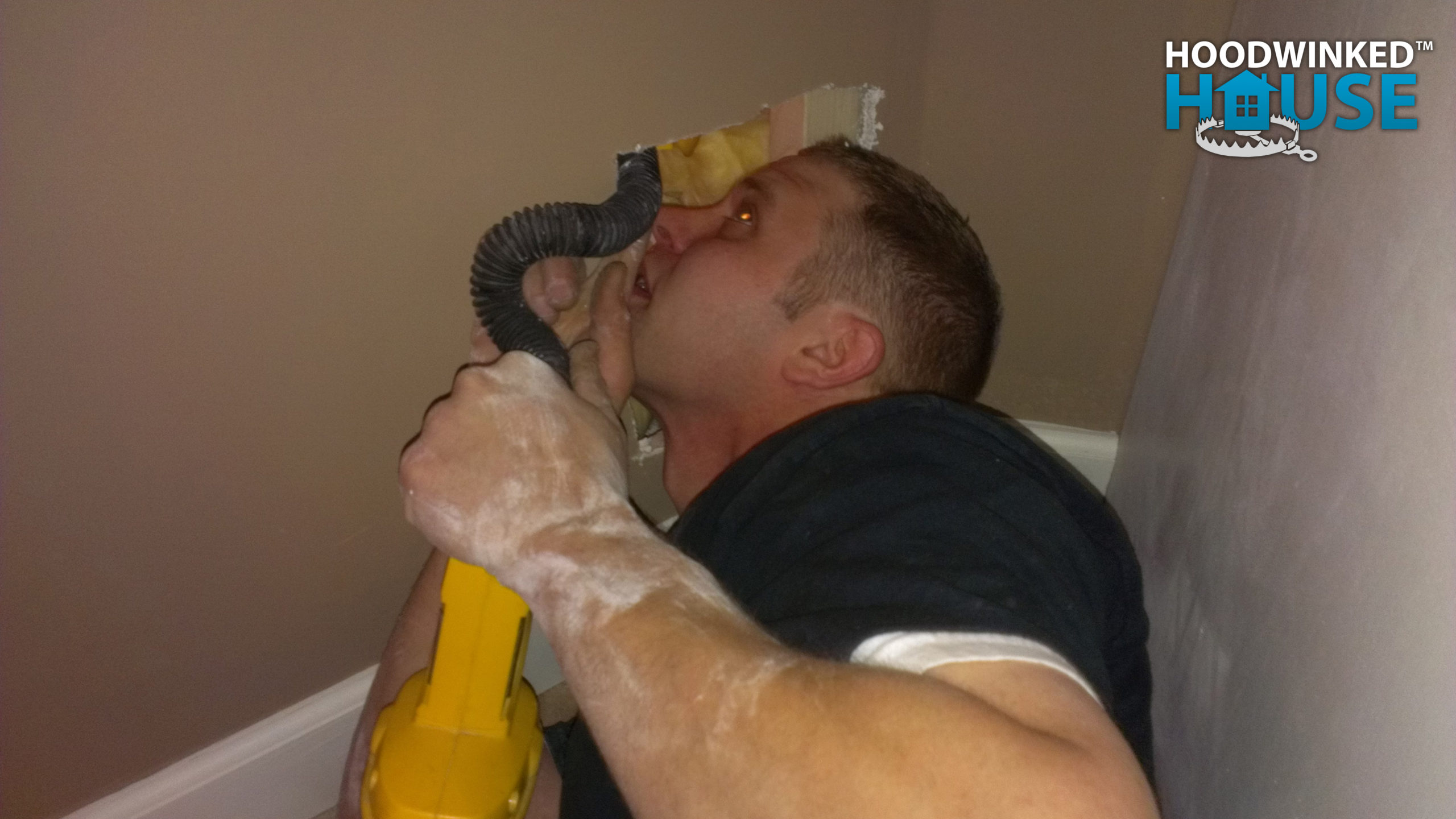 A plumber uses a flashlight to look through an inspection hole in drywall.