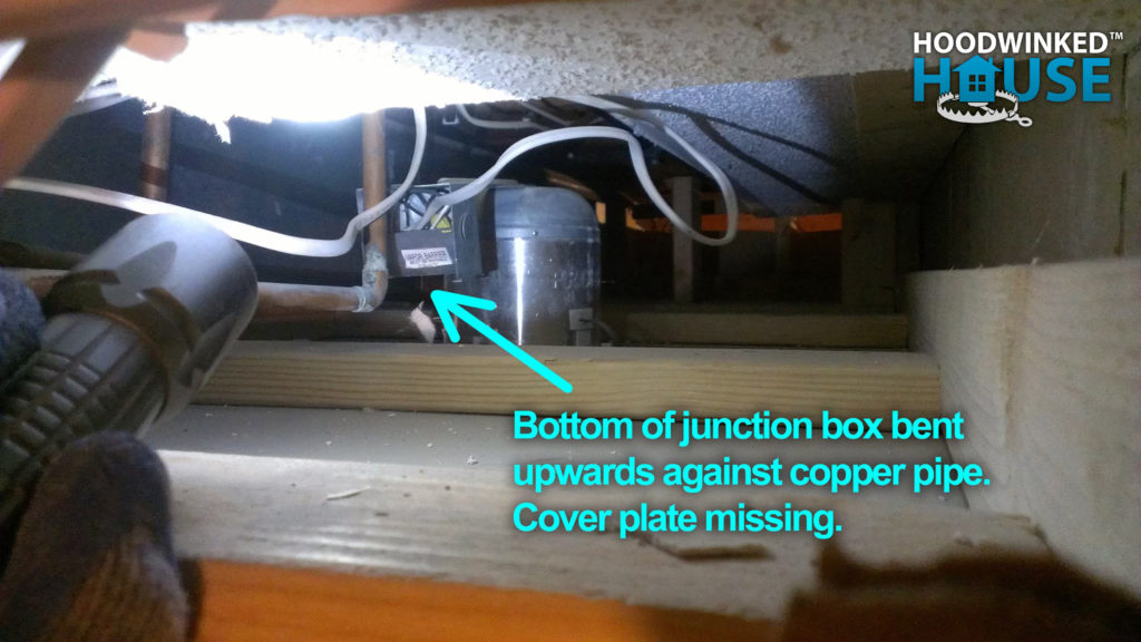 Annotated photo showing a bent junction box forced up against a copper pipe without a cover.