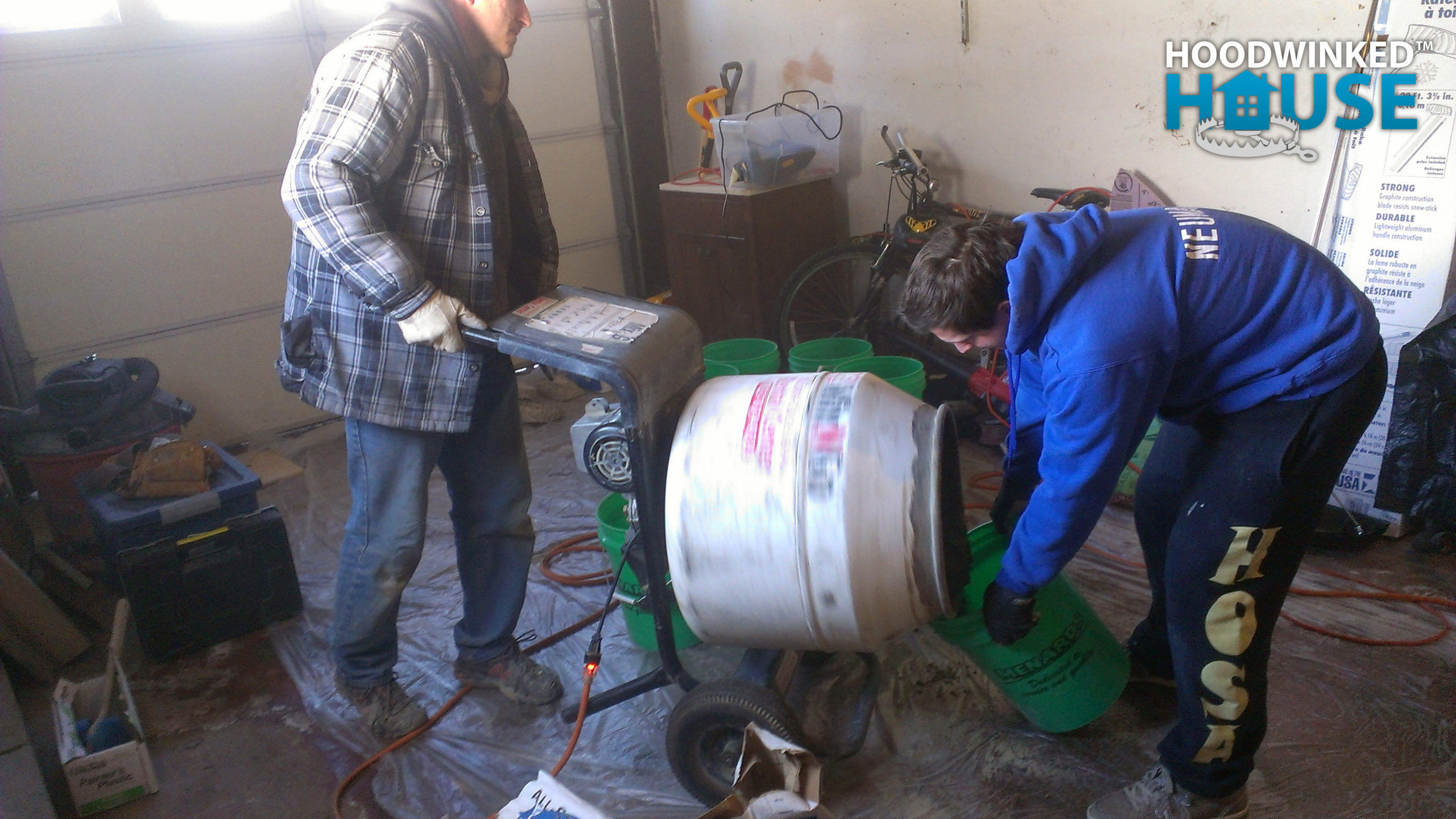 A worker dispenses concrete from a mixer while another collects it in a bucket.