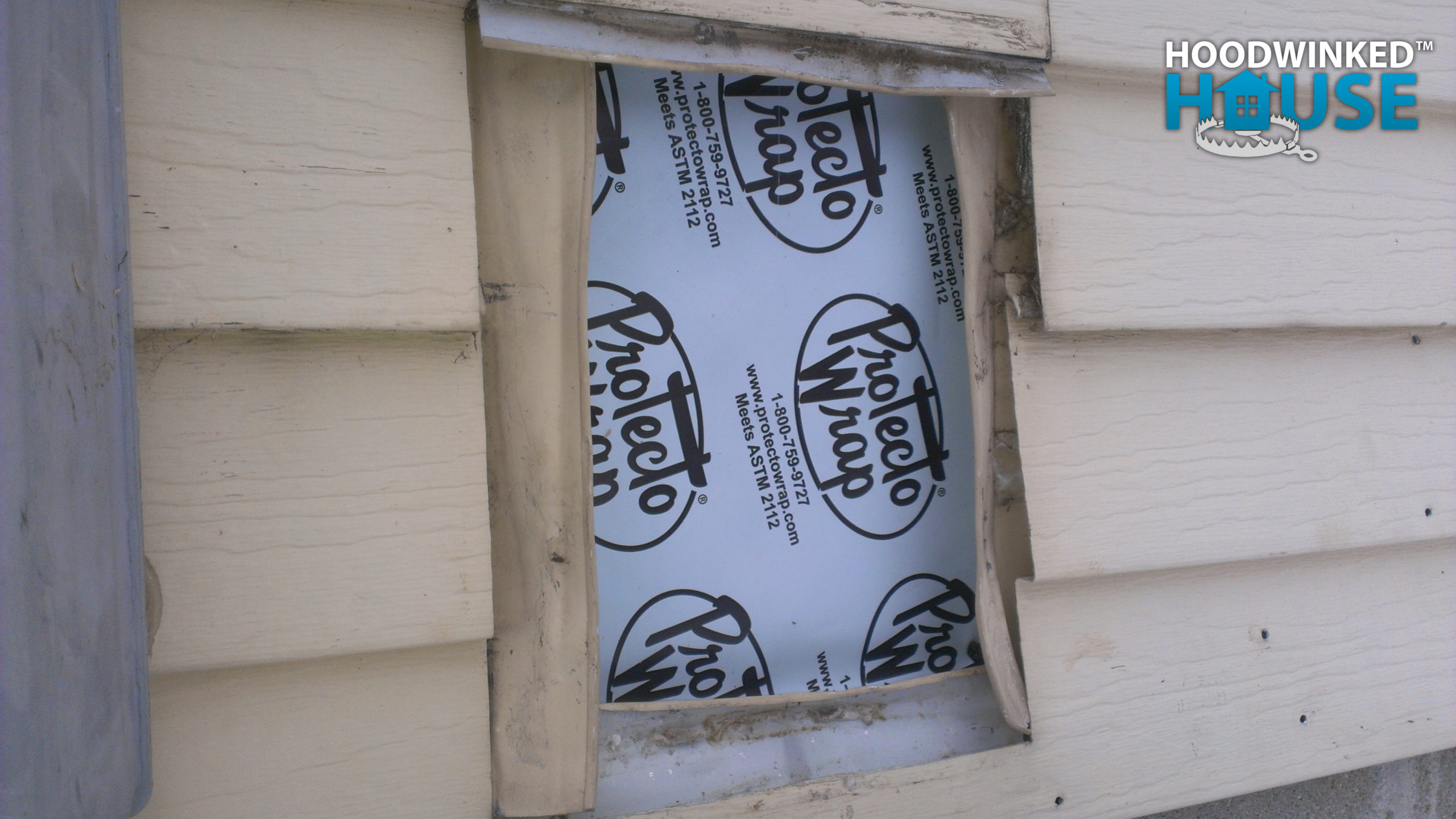An old utility hole in a house siding is sealed up with patches of self-adhesive home wrap.