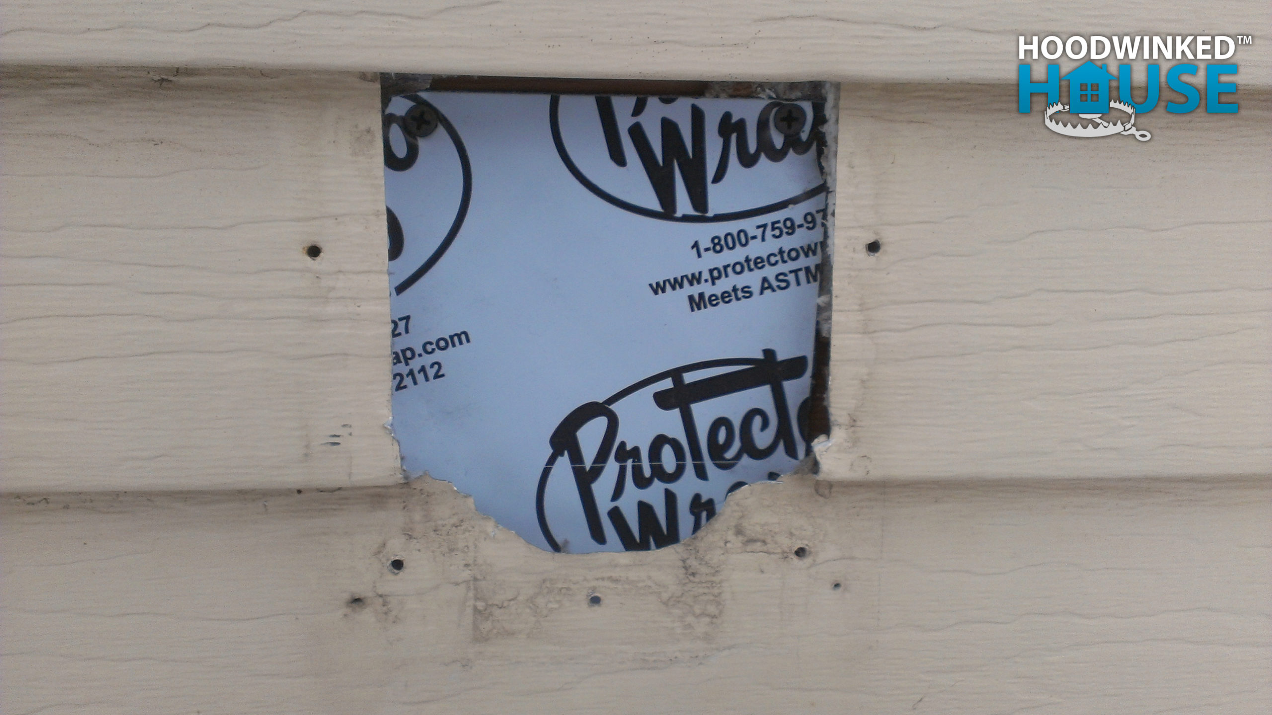 An old utility hole in a house siding is sealed up with patches of self-adhesive home wrap.