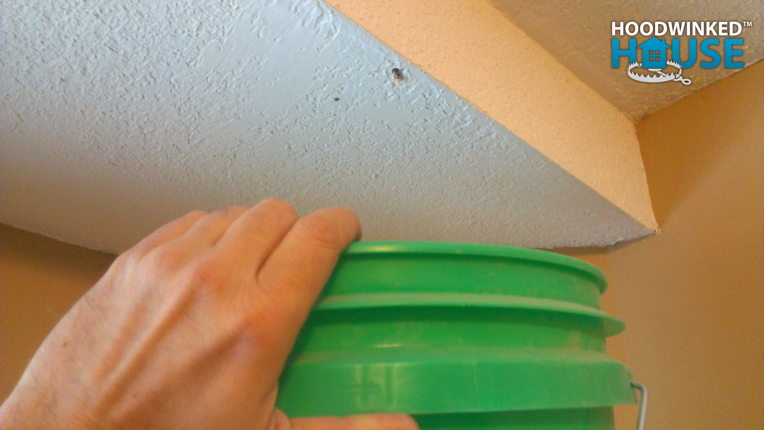 A bucket is held up to a small hole in a ceiling that is leaking water from ice dams.