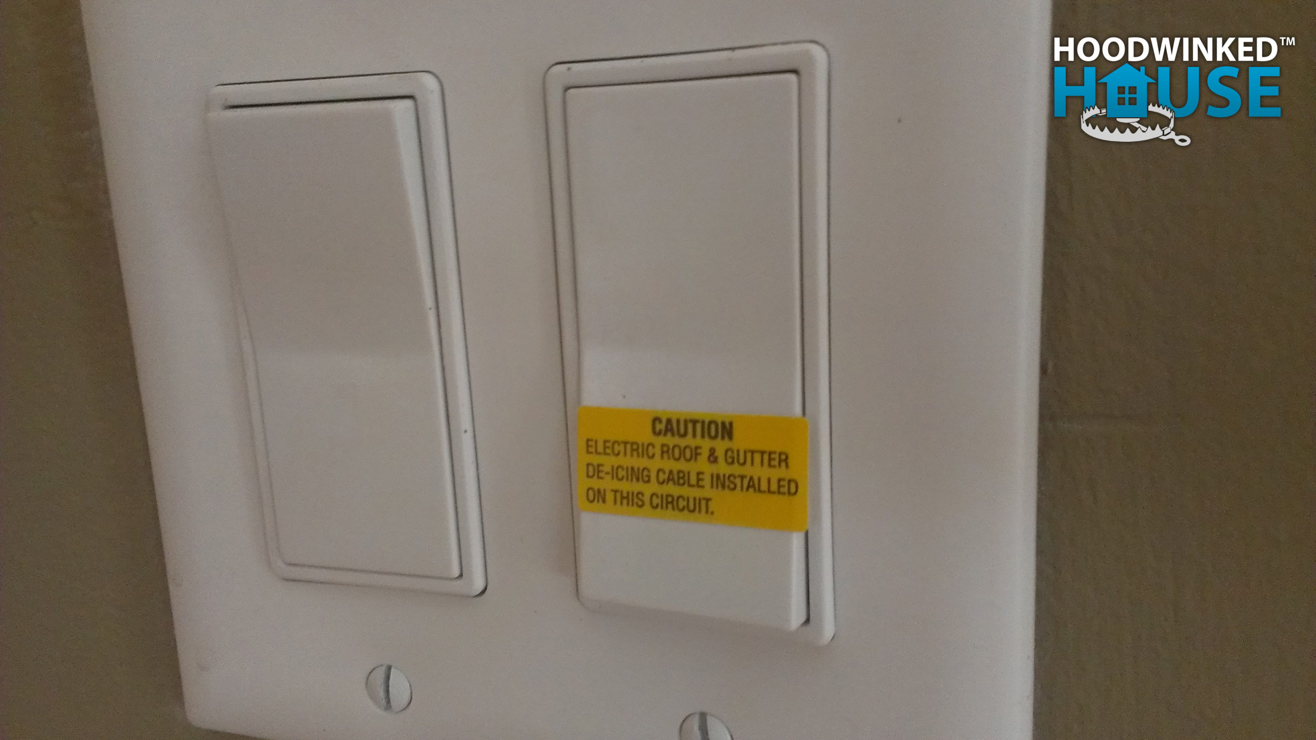 A light switch has a yellow label that says: CAUTION. Electric roof & gutter de-icing cable installed on this circuit.