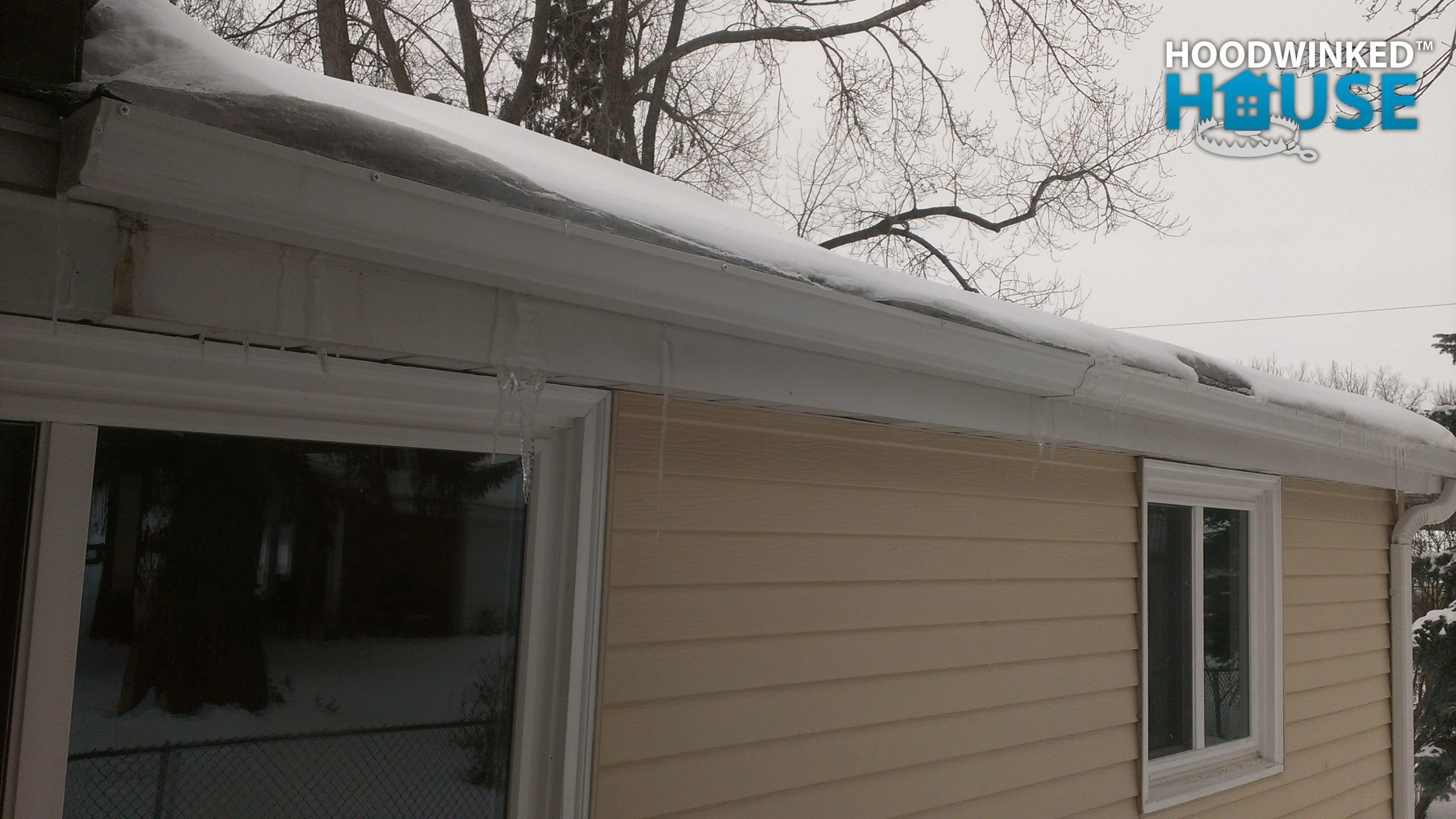 Icicles form beneath a snowy gutter that is forming ice dams.