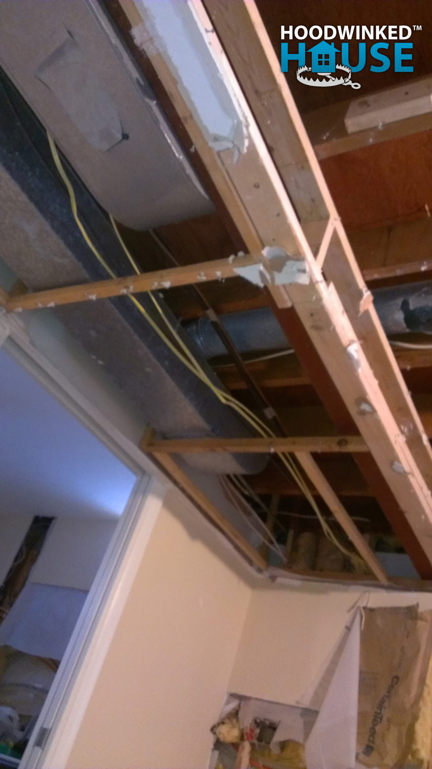 Ceiling drywall removed from a bedroom soffit reveals a heating duct with a flap hole cut in it.