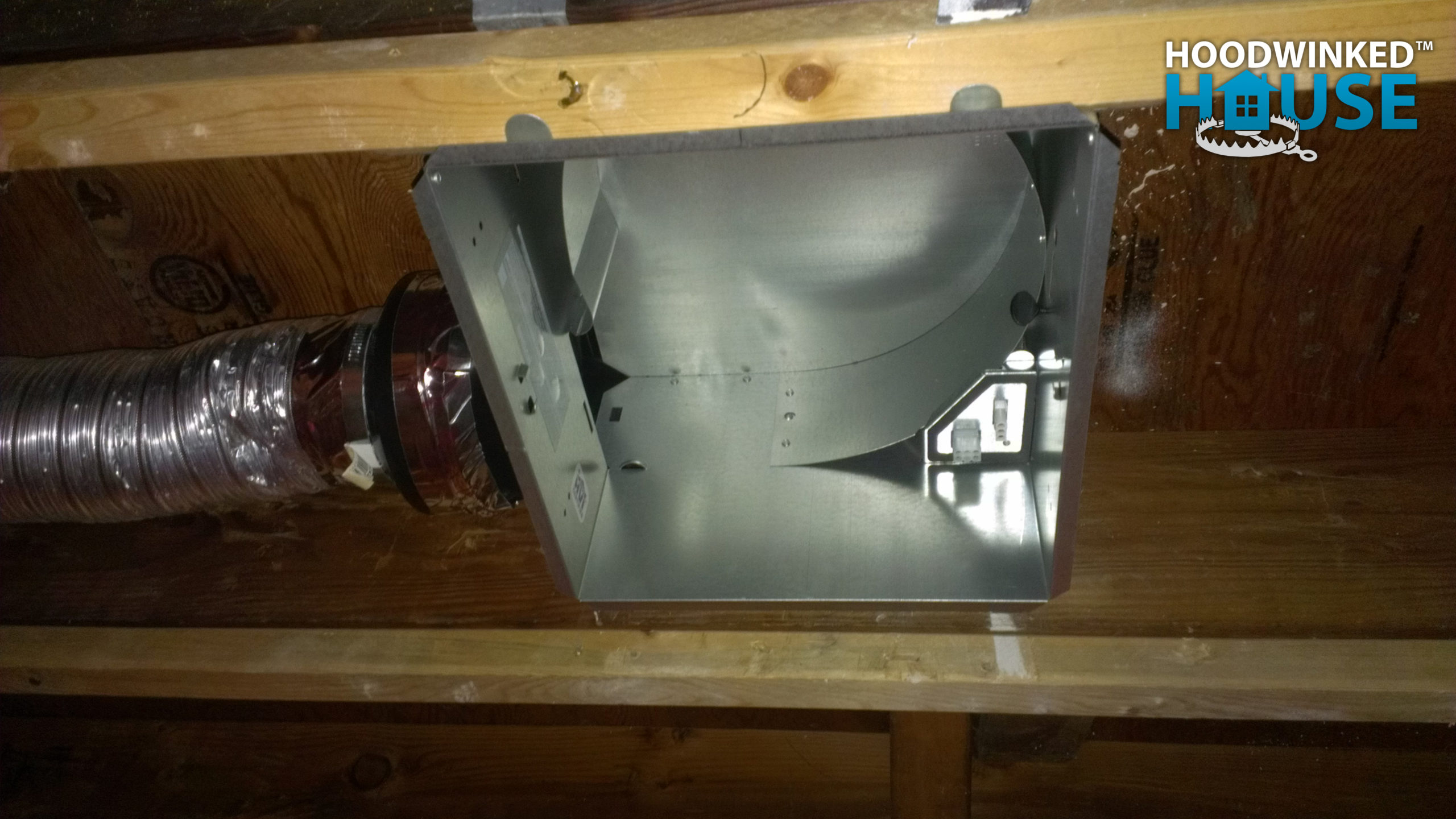 The housing for a bathroom fan is installed between ceiling framing.