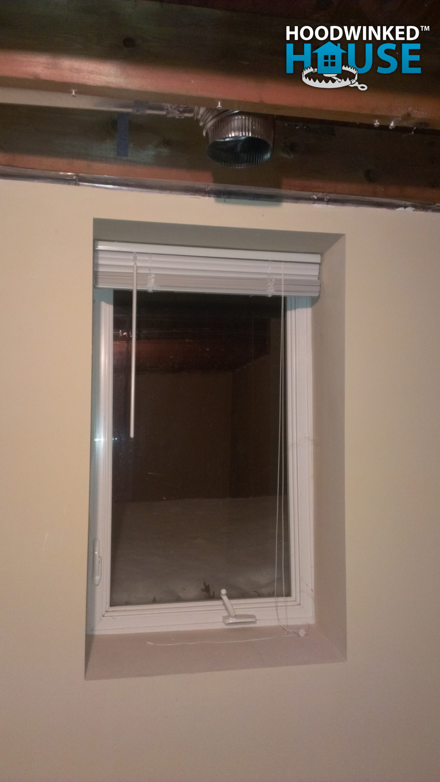 An basement ceiling air duct branch ends in an elbow above a window.