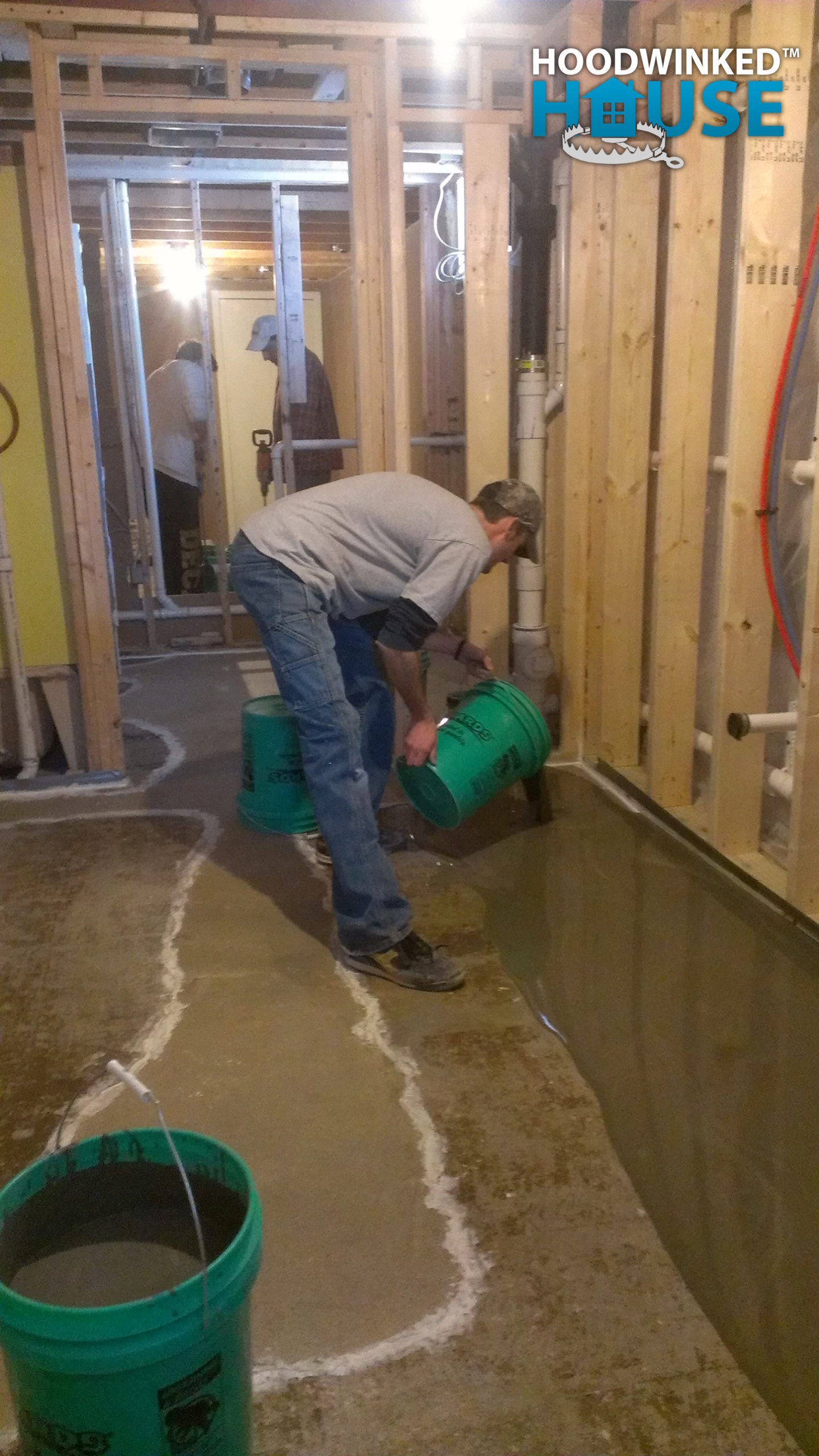 A worker pours self-leveling concrete from a bucket onto a basement floor.