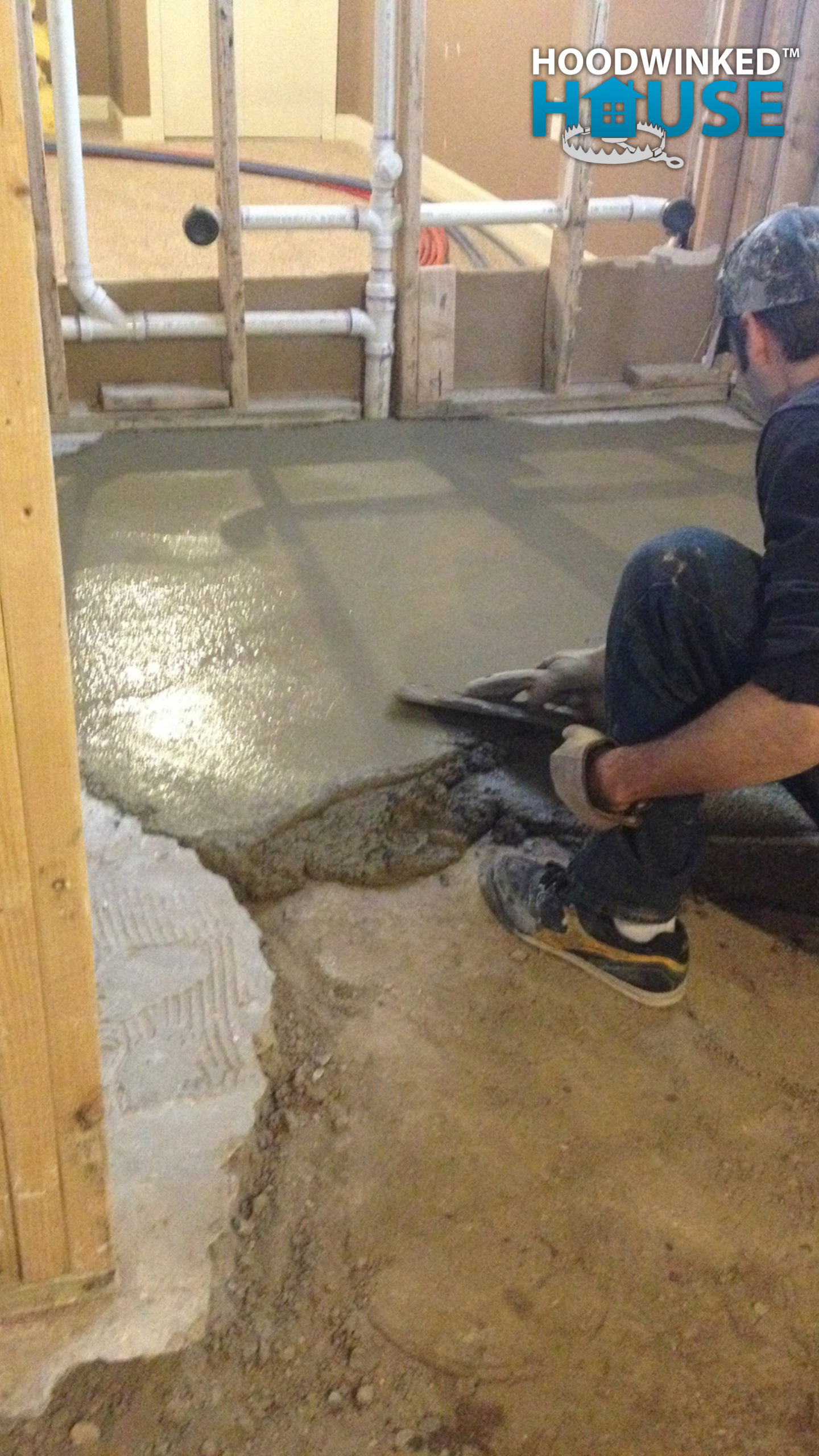 A worker lays new concrete over bare earth in a basement where part of the original floor had been removed.