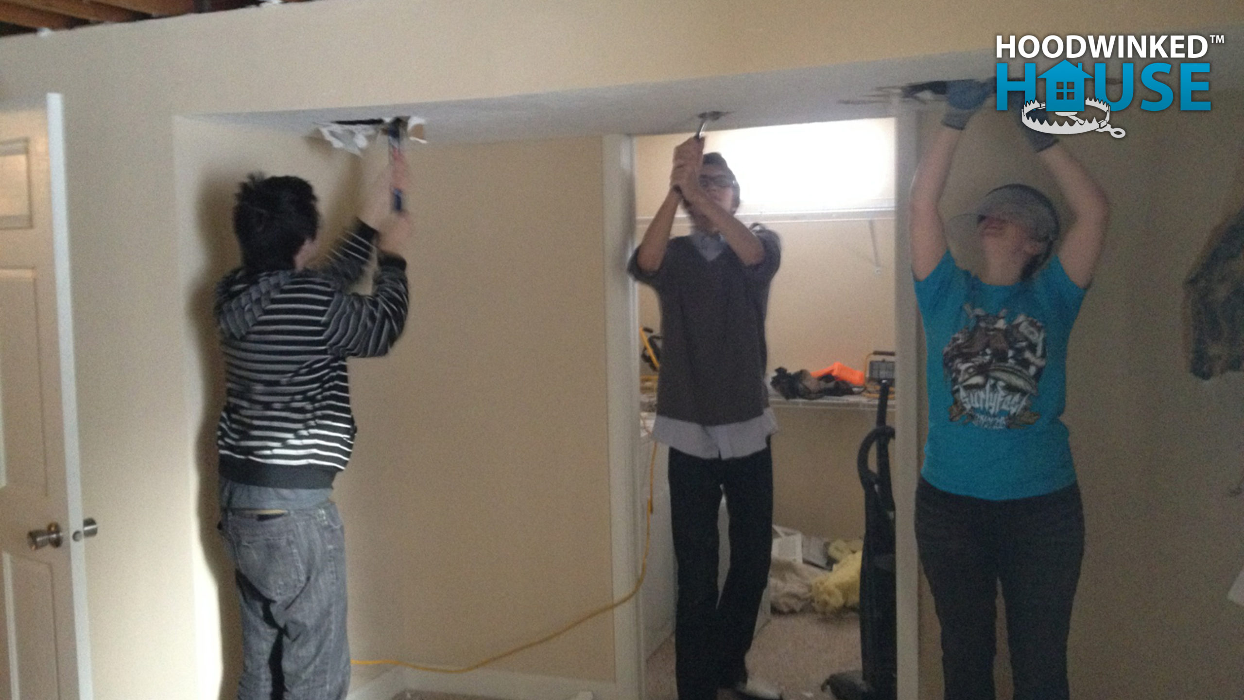 Three people using prybars to demolish drywall from a bedroom ceiling.