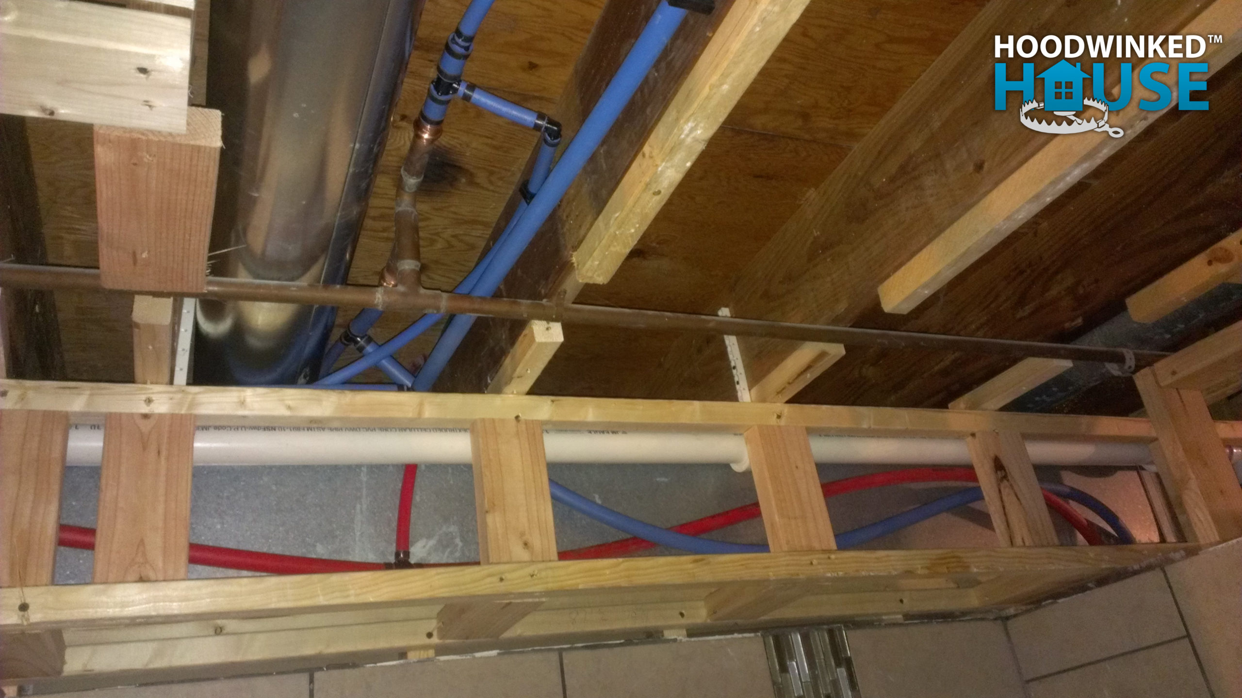 Blue and red Pex pipes interconnect with legacy copper pipes in a basement ceiling.