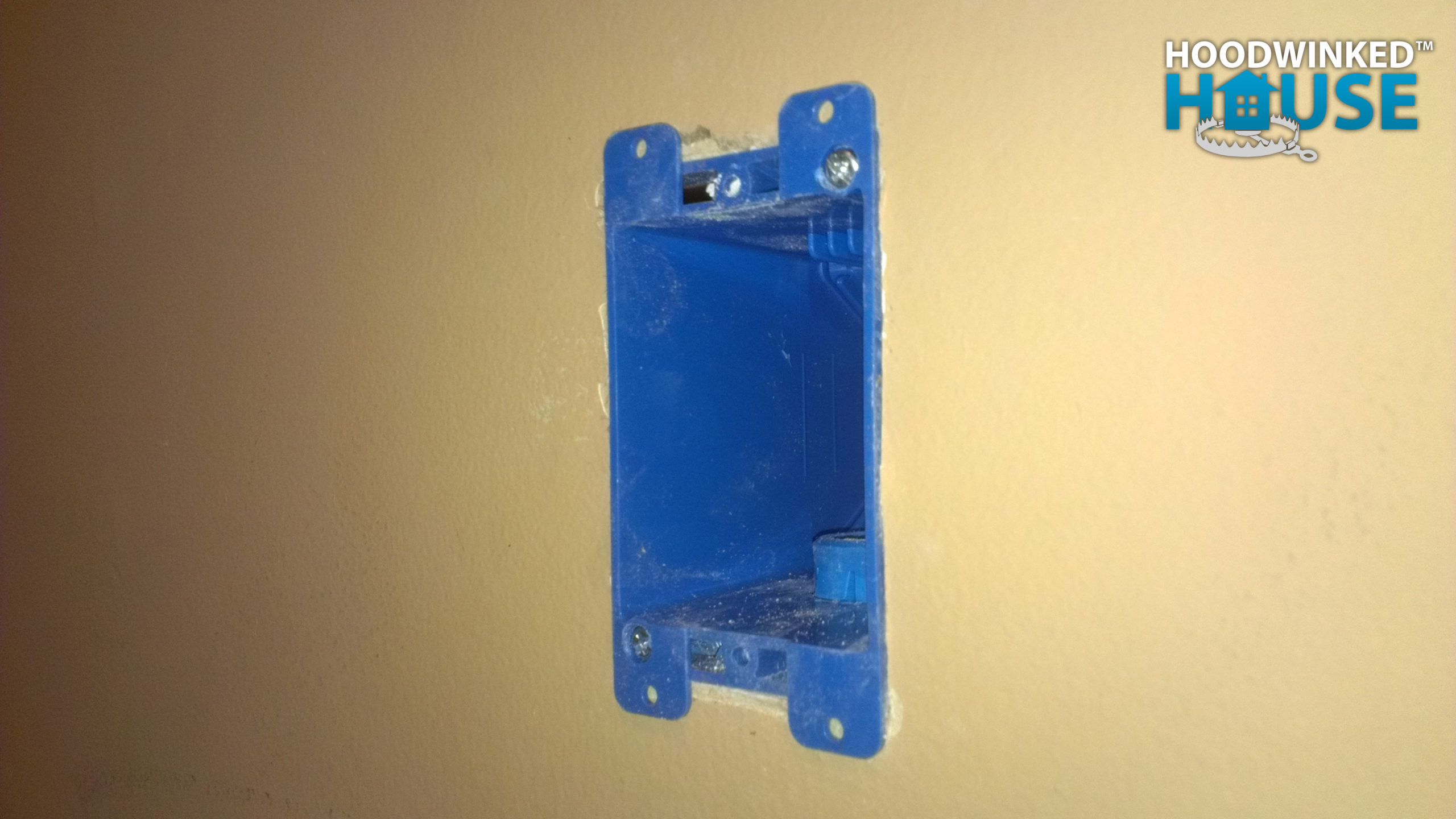 A blue old work junction box is installed in drywall. It has been modified to include a PVC conduit connector.