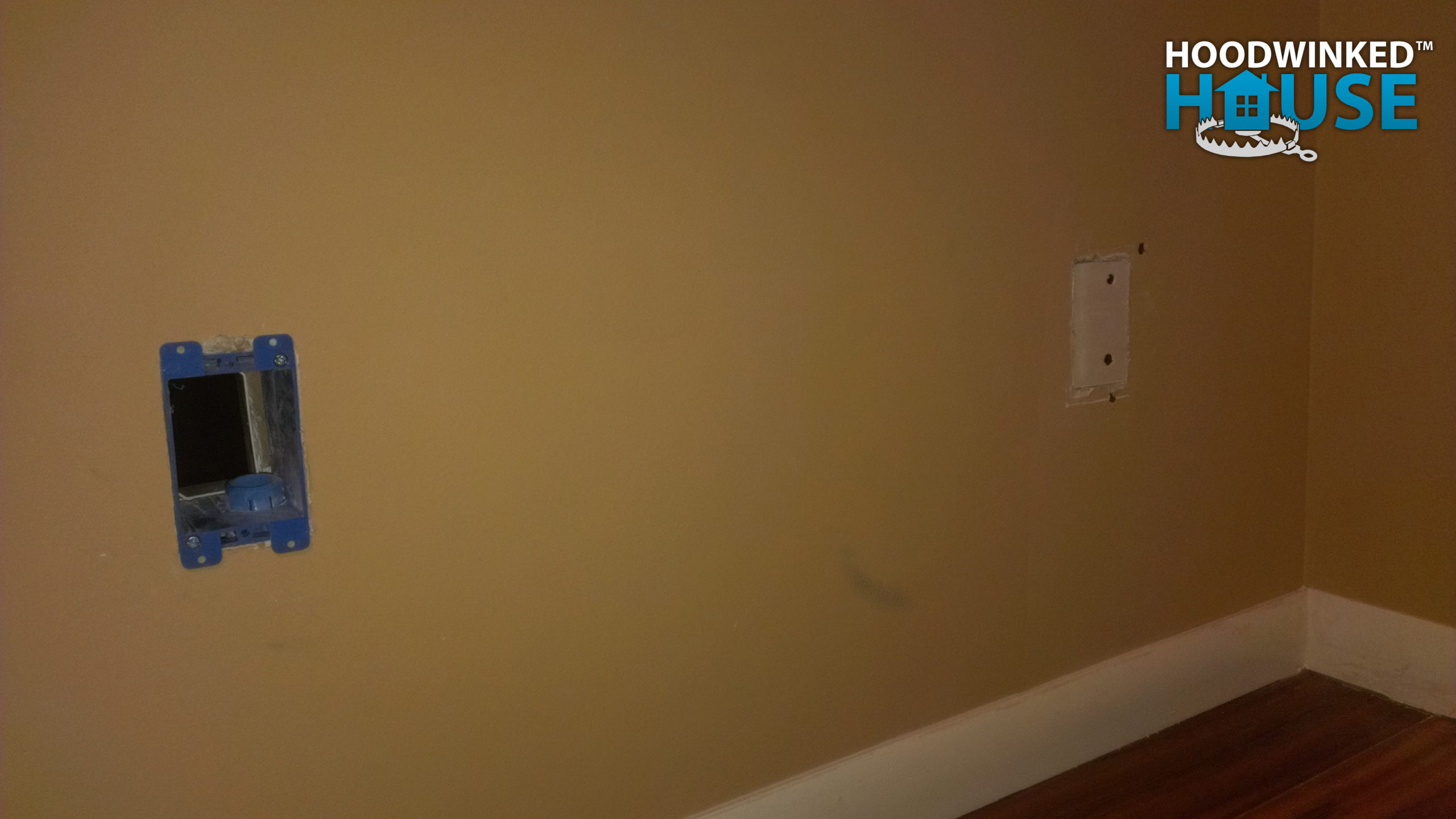 A bedroom wall with holes for junction boxes, one patched with drywall.