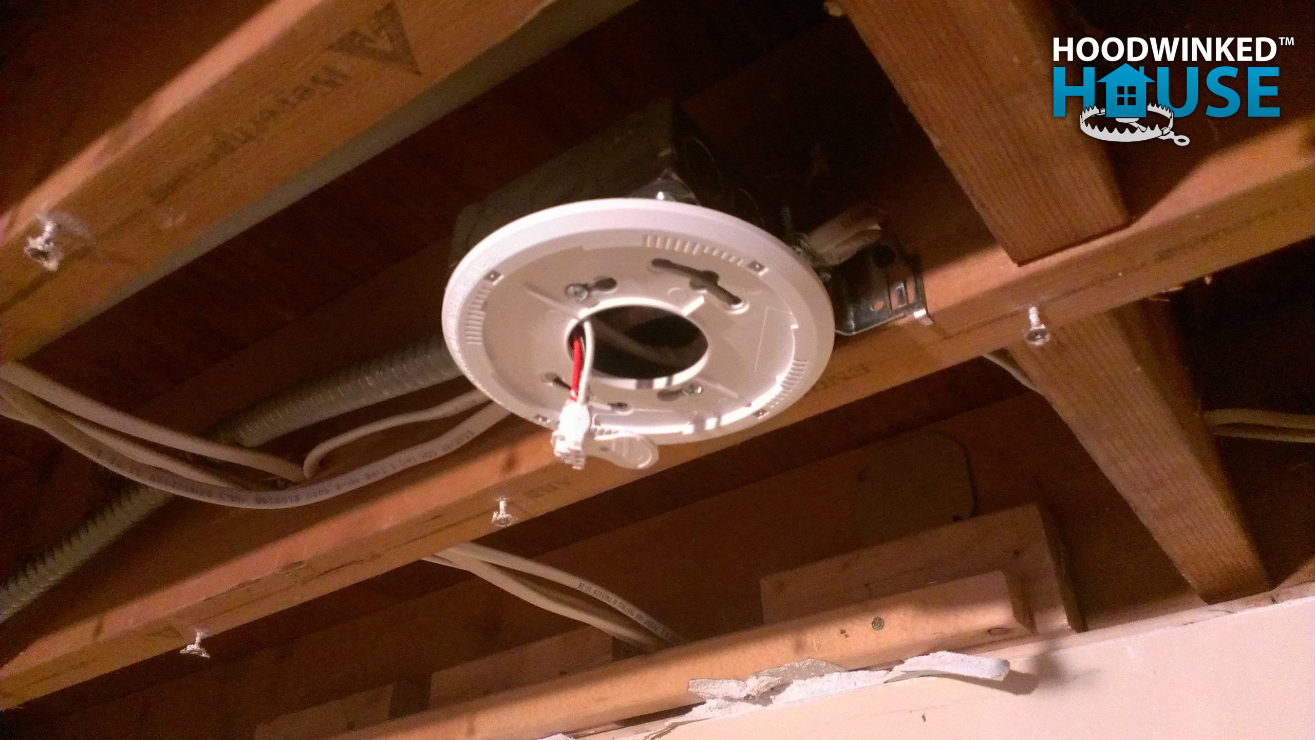 New construction smoke alarms must be interconnected per building code. A mounting plate is shown here wired into a basement ceiling junction box.