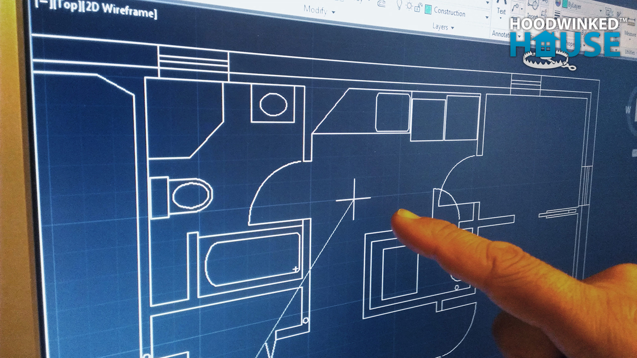 A hand points to CAD floor plans on a computer screen.
