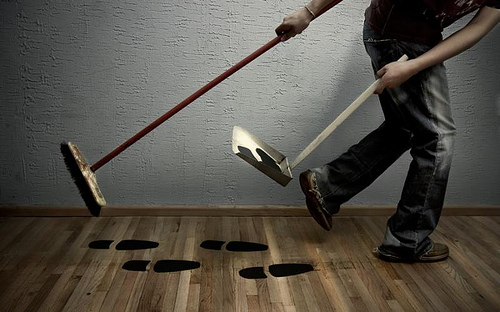 A person sweeps up their own footprints with a broom and dustpan, illustrating how a flipper covers up their involvement with predatory remodeling.