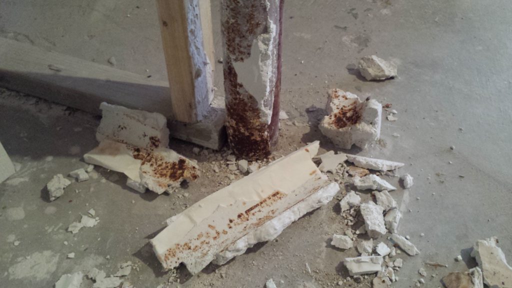 Drywall mud was applied to this steel support column causing it to rust. Thick chunks of the dried mud have been broken away from the column and lay on the basement floor.