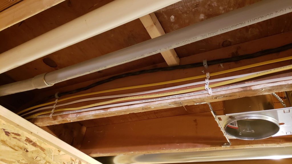 A series of electrical wires are neatly fasted to a joist with wire staples.