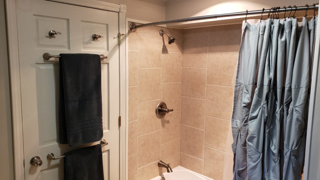 A bathroom with a tiled shower and towel bars mounted to the back of the door.