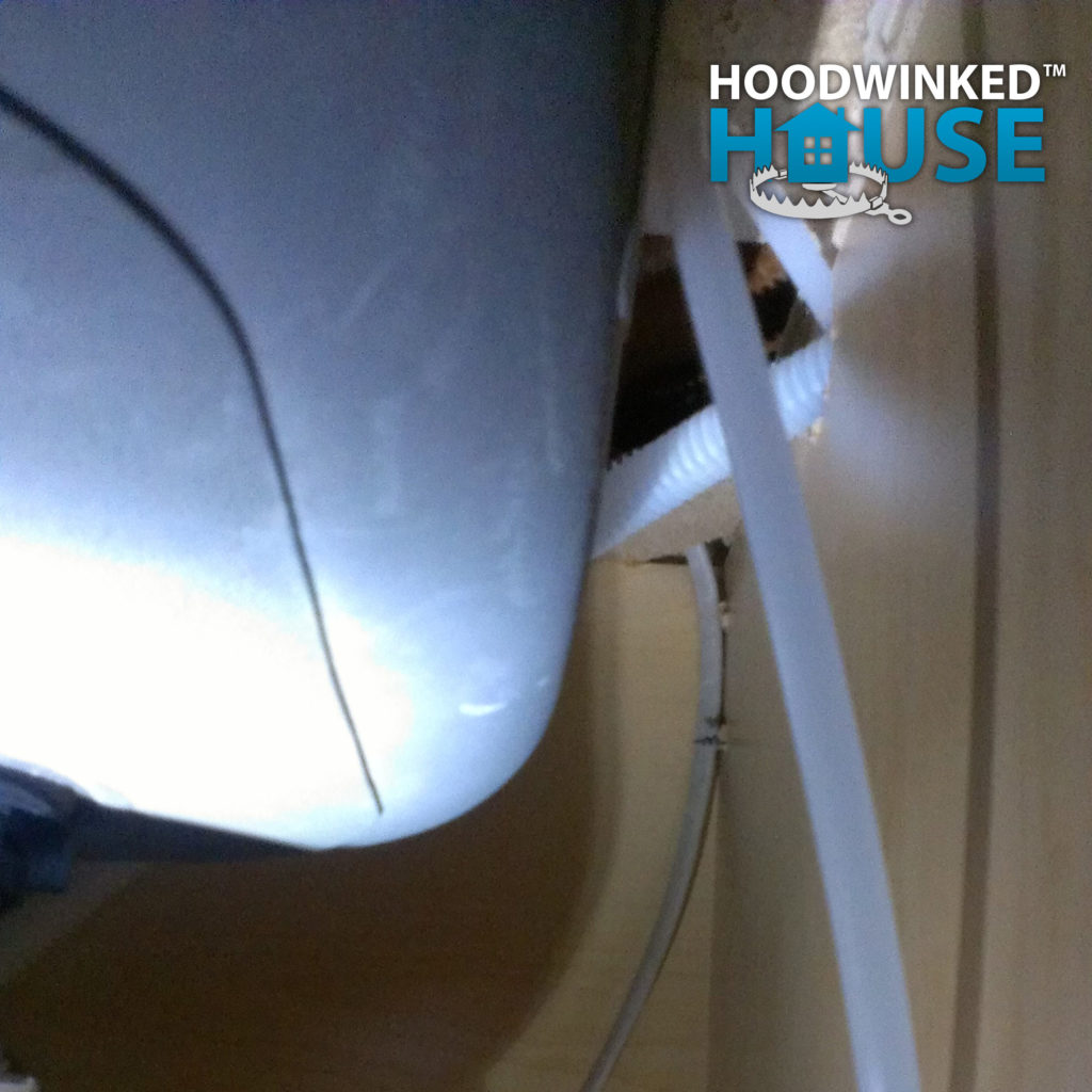 Incorrect dishwasher hoses running through a sink base cabinet.