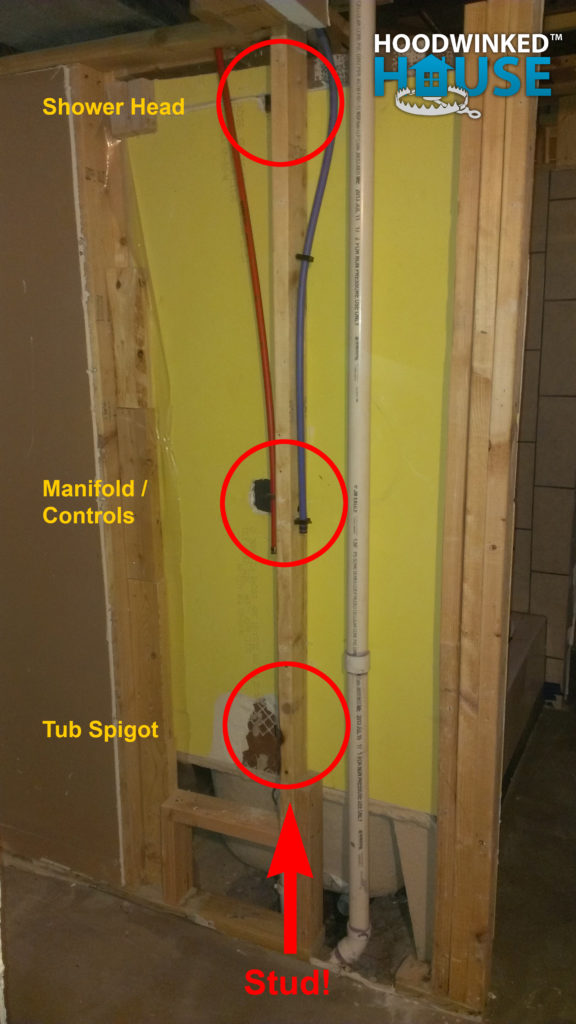 Annotated photo of framing and plumbing behind a shower where the shower head, manifold and controls, and tub spigot all are directly on top of a stud.