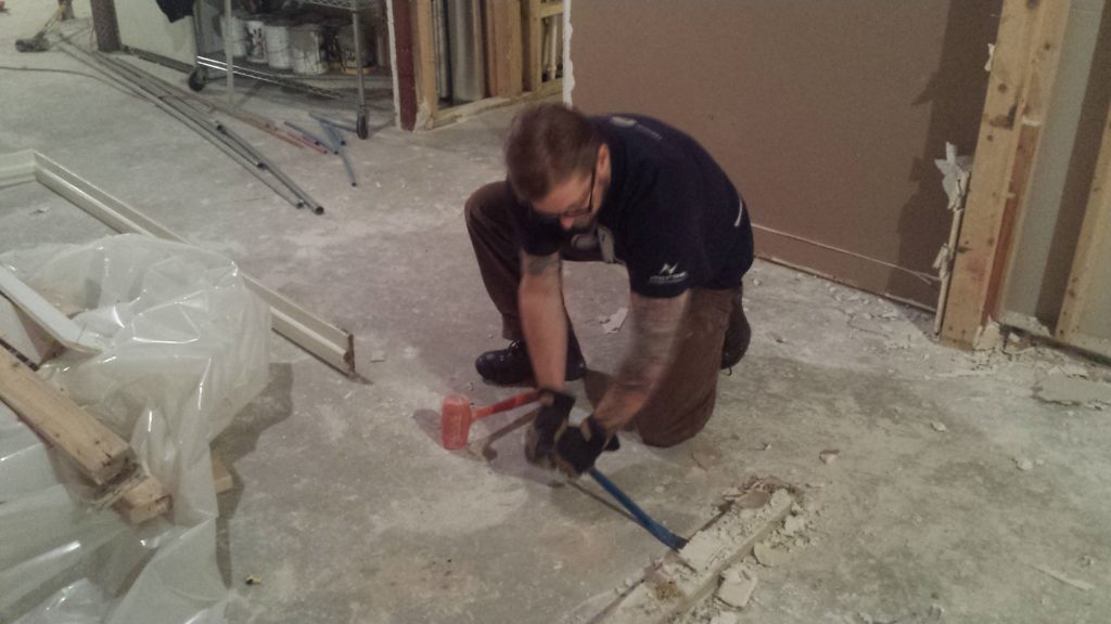 Using a prybar and mallet to remove framing that has been anchored to the basement floor.