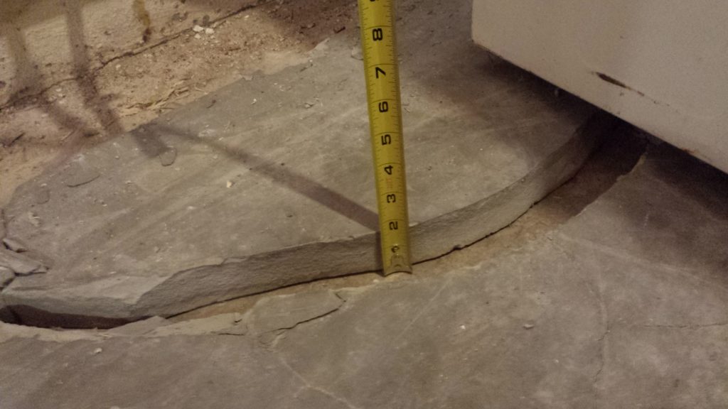 Self-leveling concrete that was poured too thick has cracked and broken away from the rest of the floor. A tape measure against the piece reads 1.75 inches thick.