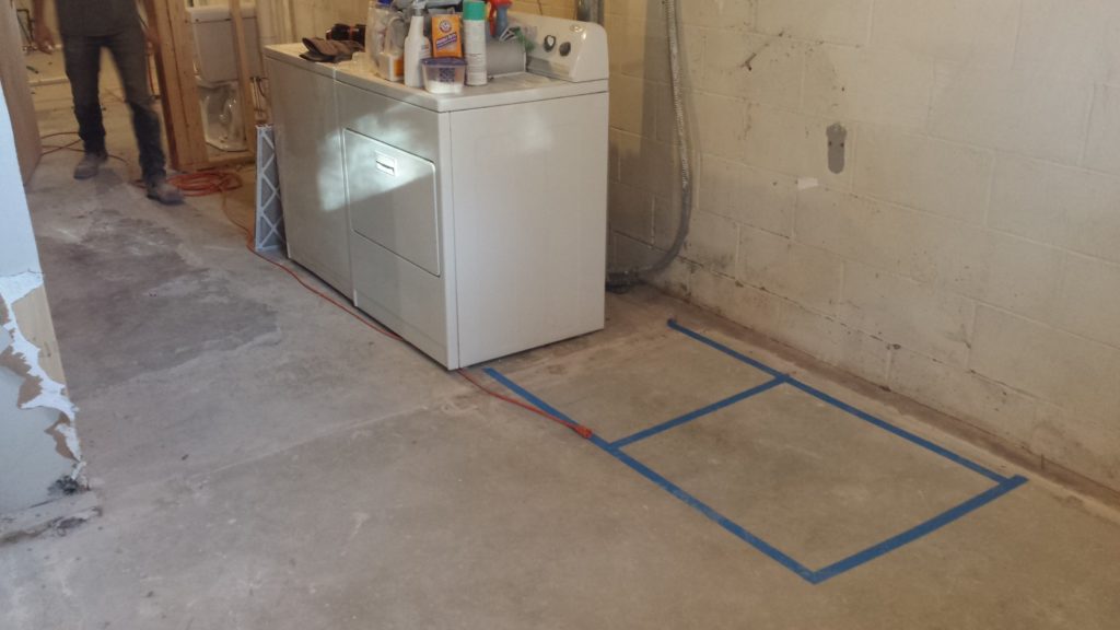 Basement laundry room floor marked with tape where the appliances will ultimately sit.