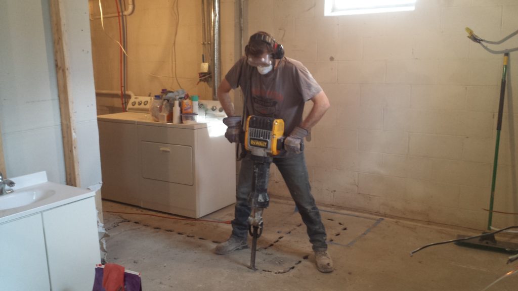 Using a jackhammer to perforate a basement floor to make trench for underground drain pipes.