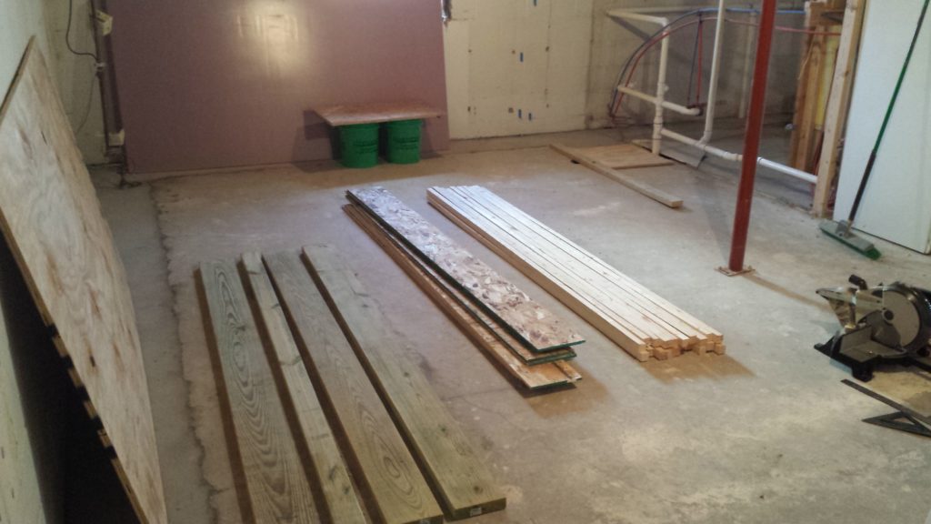 Lumber is staged on a basement floor for a construction project.