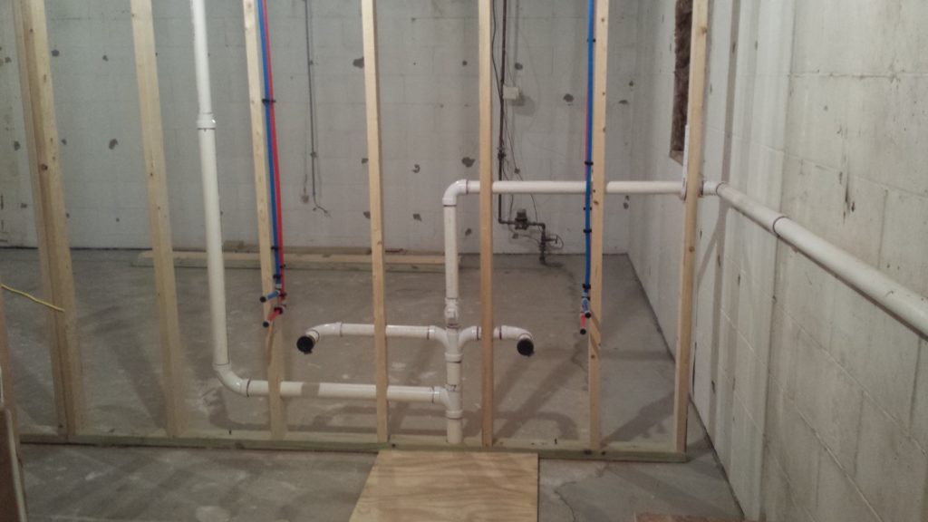 Basement bathroom plumbing rough in with drain pipes and water lines attached to a stud wall.