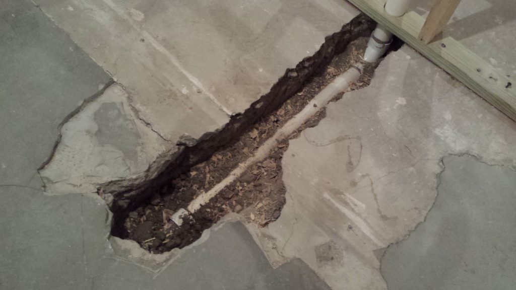 Underground drain pipe runs through a trench in a basement floor.