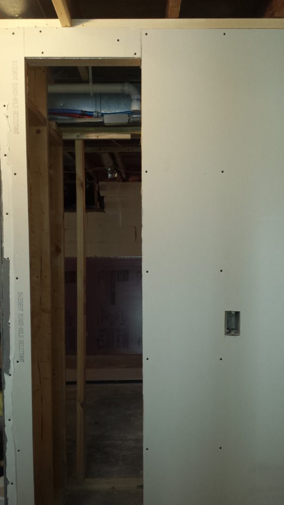 Drywall over a stud wall framed for a linen cabinet in a basement bathroom.