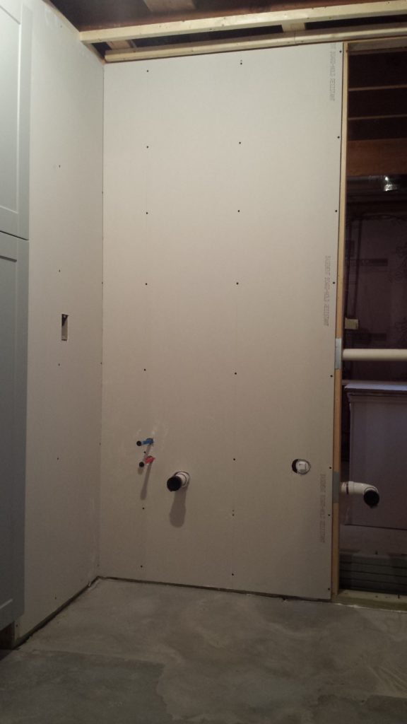 Drywall is added to a basement bathroom stud wall with allowanced for the plumbing.