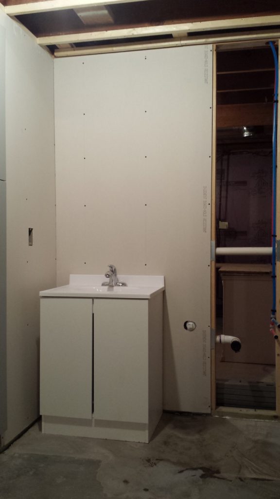 A temporary sink is installed in an unfinished basement bathroom.