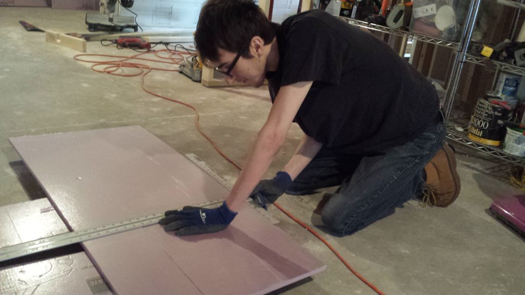 Harry measures and cuts foamboard insulation for the basement rim joist.