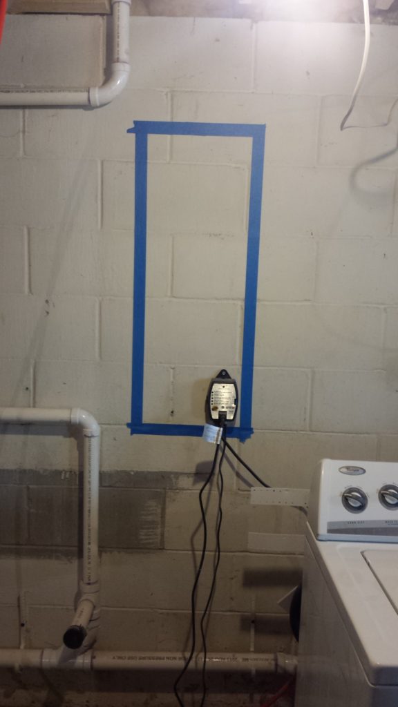 Tape marks the location of a future electrical service panel on a basement wall.