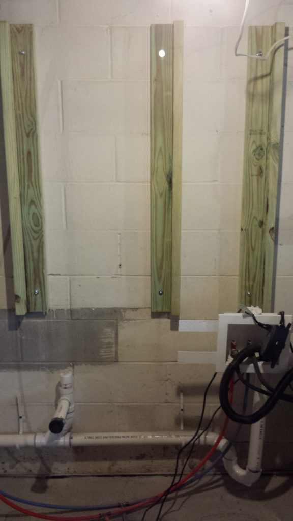 Framing for a pair of electrical service panels is anchored to a basement wall.