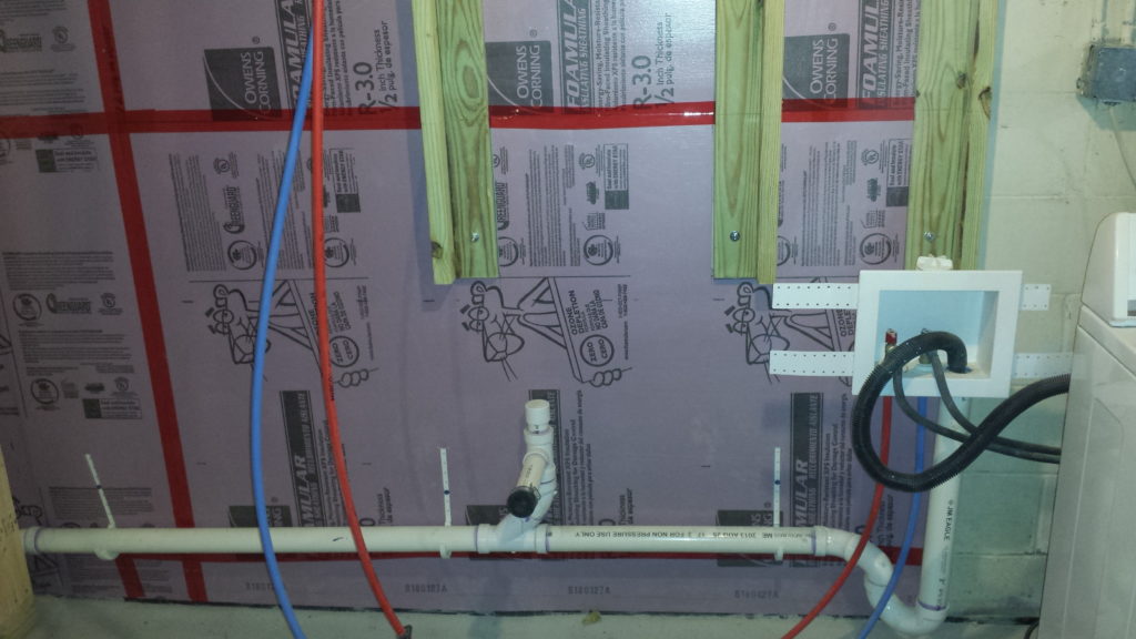 Insulation is added to a basement wall around some framing for a pair of electrical service panels.