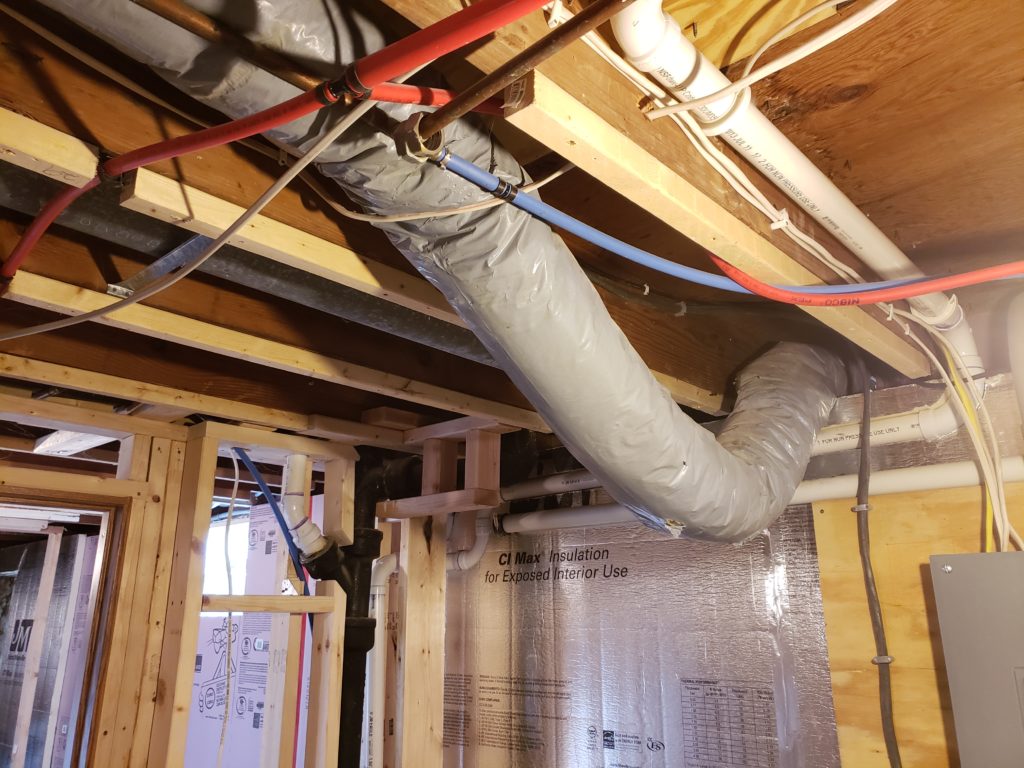 A flexible fresh air intake hangs from a basement ceiling, sagging in the middle.