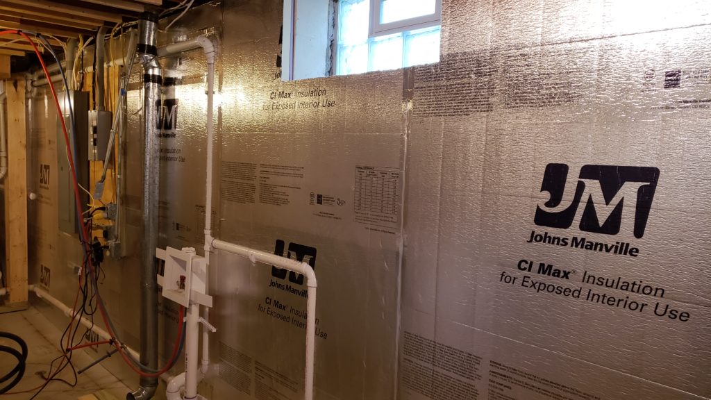 Foil faced foamboard insulation cut to match laundry pipes on a basement wall.