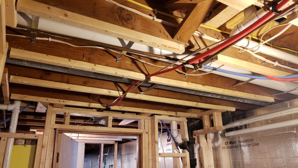 A PVC fresh air duct between joists in a basement.