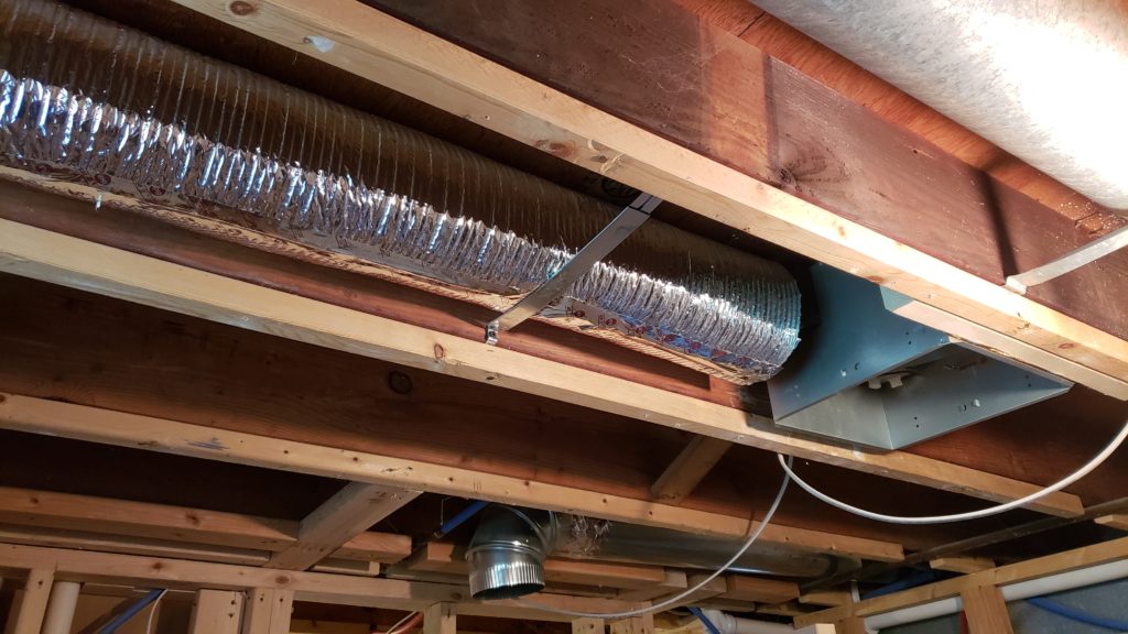 A bath fan housing with a large duct in the ceiling joists of a basement bathroom.