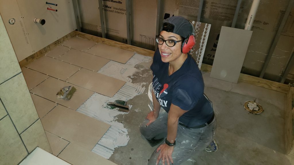 Amáda lays new tile on the basement bathroom floor.