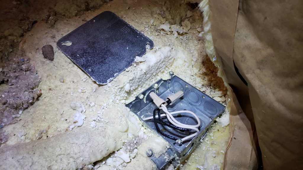 An attic junction box that has been dug out of spray foam insulation.