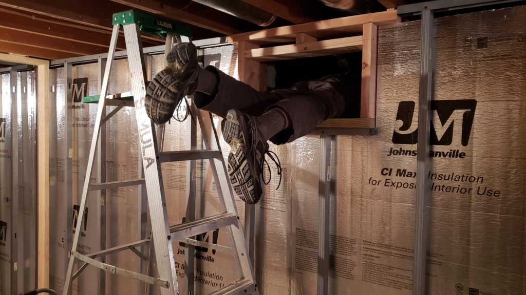 Using a ladder to climb through a small basement window into a crawlspace.