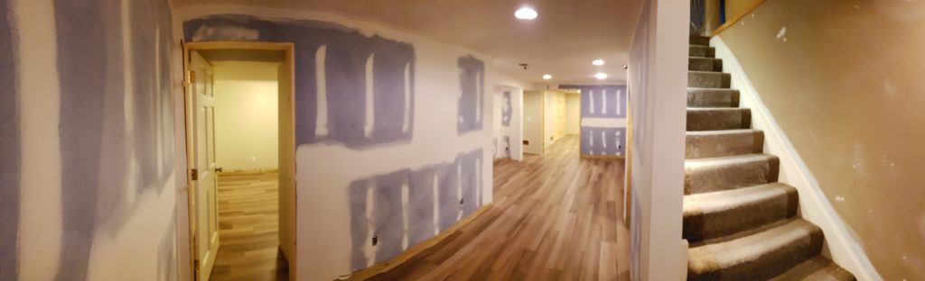 Panorama of wood grain vinyl flooring planks in an unfinished basement.