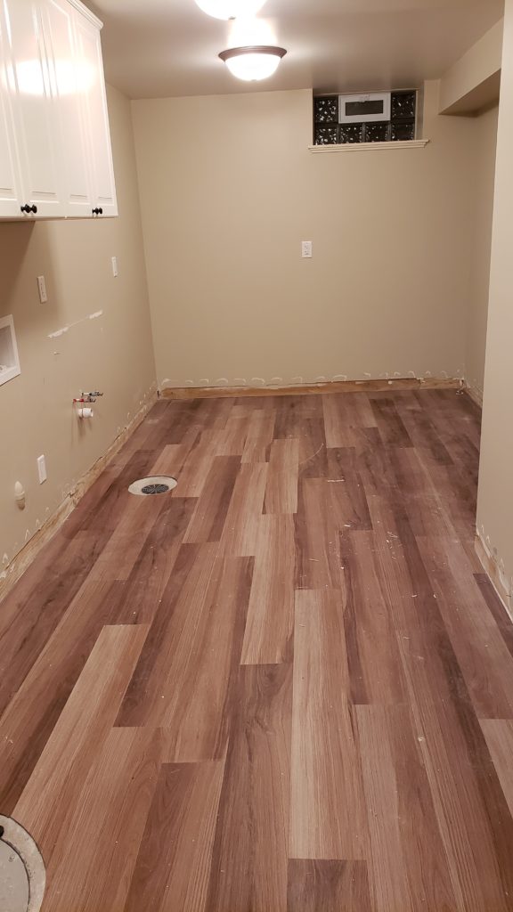 A finished basement laundry room that has been prepared to have the vinyl flooring removed.