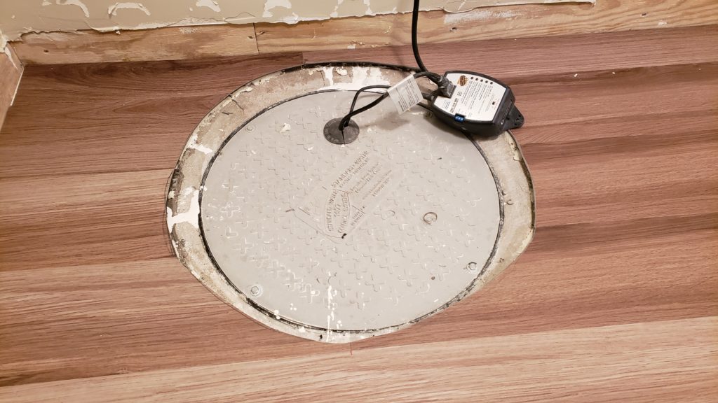 Vinyl flooring around a round sump pump cover with sloppy, uneven edges.
